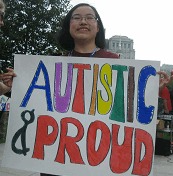 Young East Asian person holding a sign with the words “Autistic and Proud”.